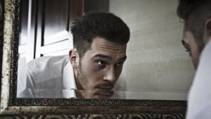 Young man bent over sink, looking into mirror